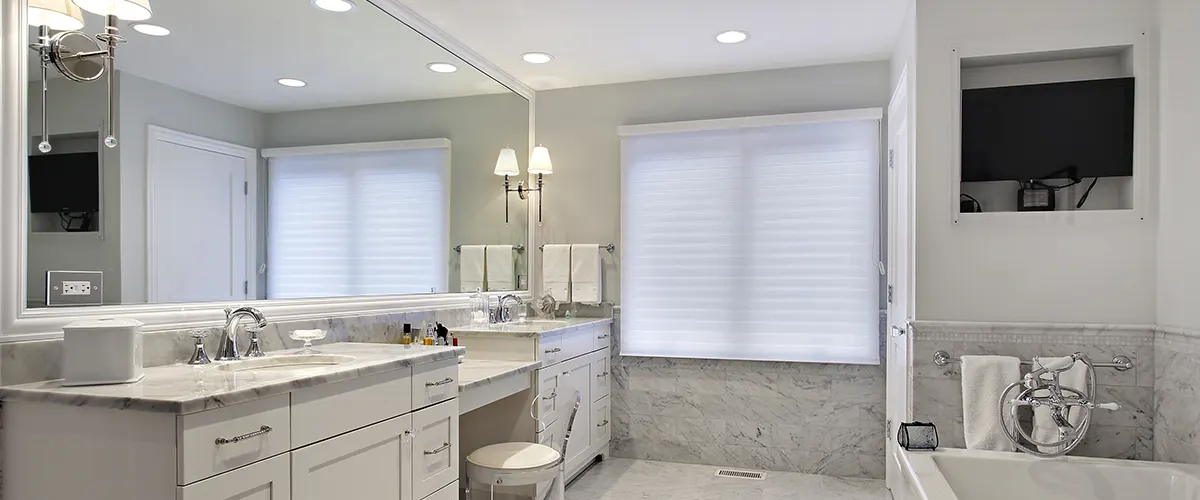 Large bathroom renovation with light gray walls, white vanity with large makeup mirror, and recessed lights
