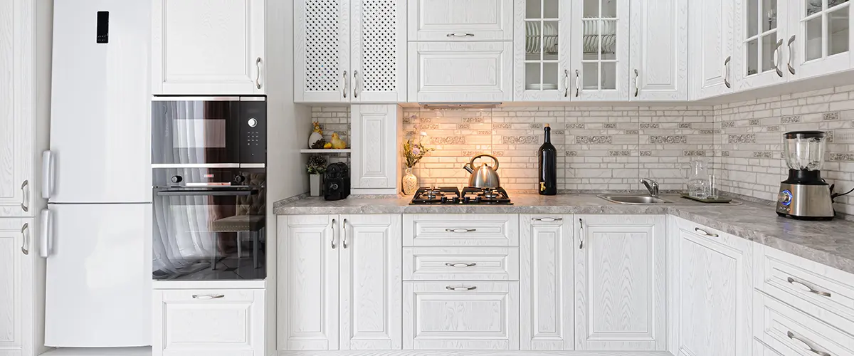 Large kitchen with white cabinets, oven and microwave tower, and stone backsplash with under-cabinet lighting