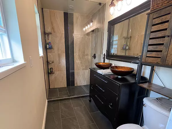 Bathroom after renovation with new walk-in shower and marble tile with black and gold accents