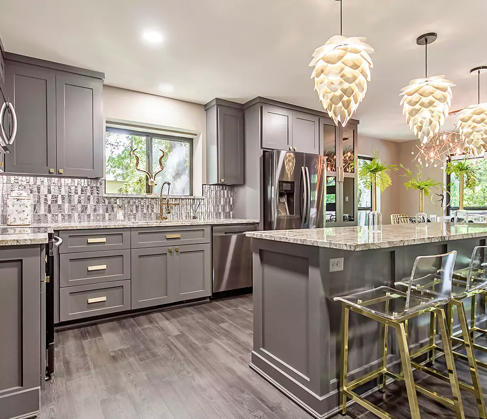 Luxurious kitchen renovation with gray cabinets, elegant overhang lights, and golden chairs and accents