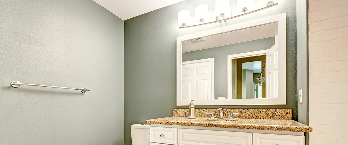 Simple bathroom with dusty green walls, white vanity, and large mirror