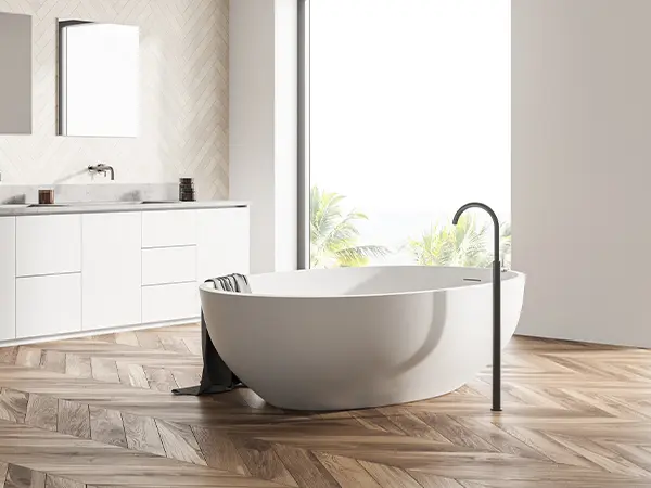 Freestanding tub in a modern bathroom with herringbone wood flooring and large window