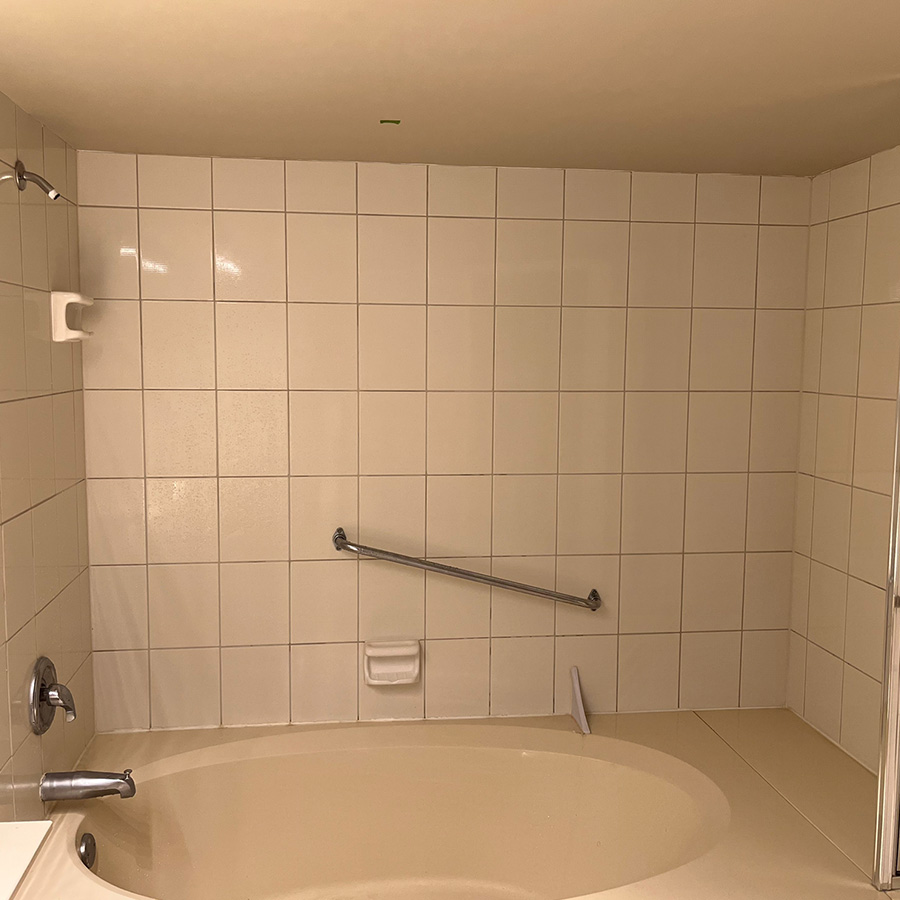 A framed bathtub with tile surround and handle bar