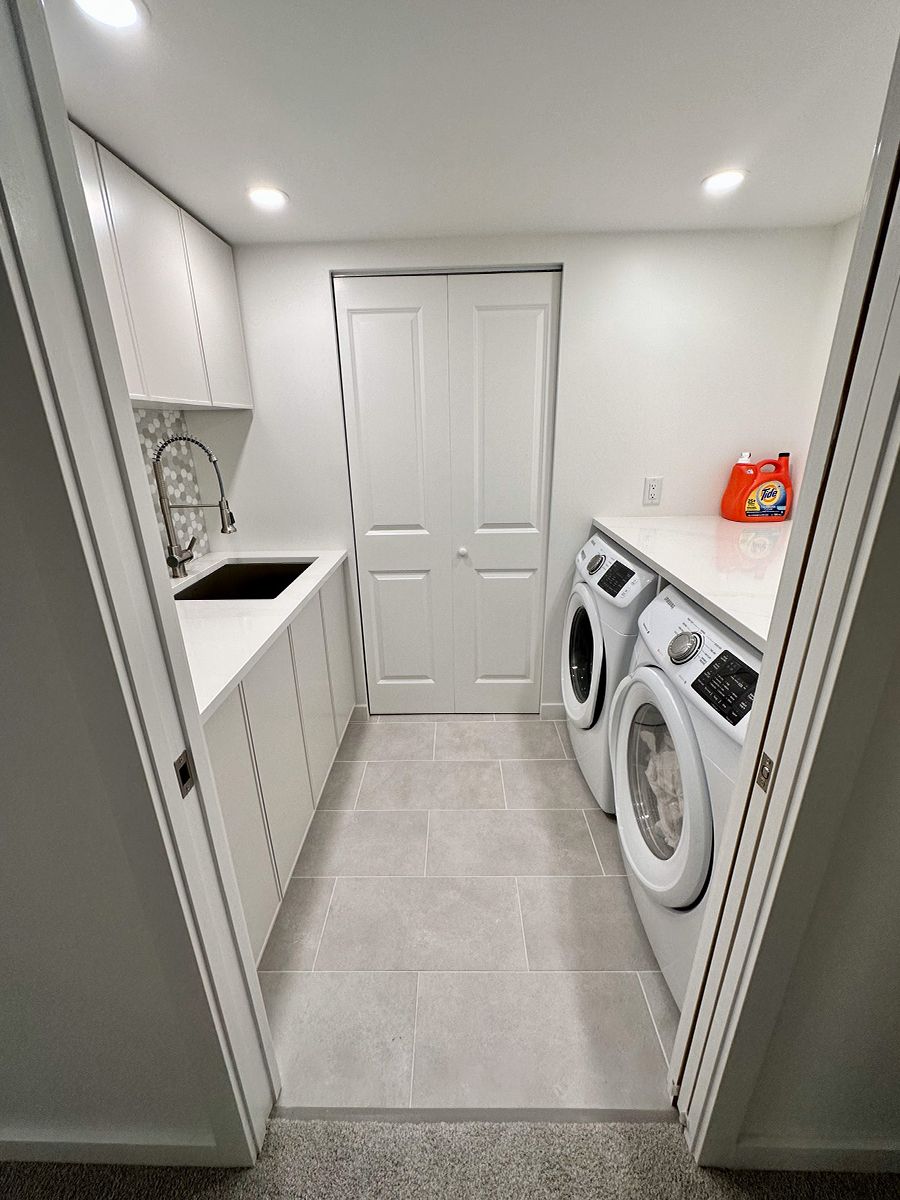 A laundry room with two washers and modern white cabinets