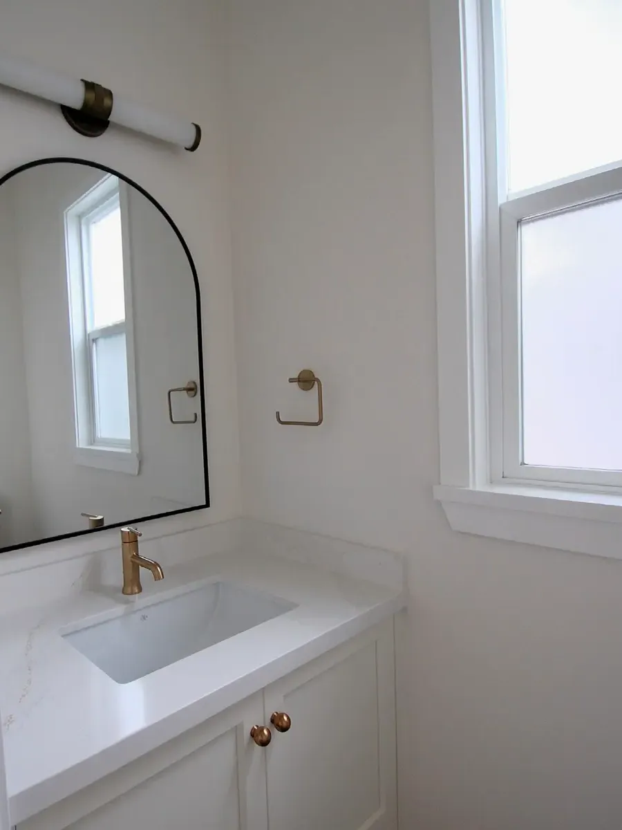 An arch mirror with black frame above a white vanity