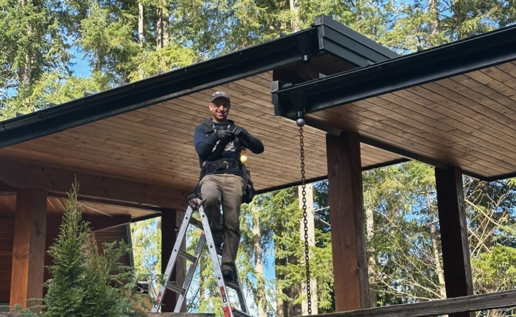 Roofer on ladder inspecting a home's roof in a forested area, emphasizing safety measures for holiday lighting installation.