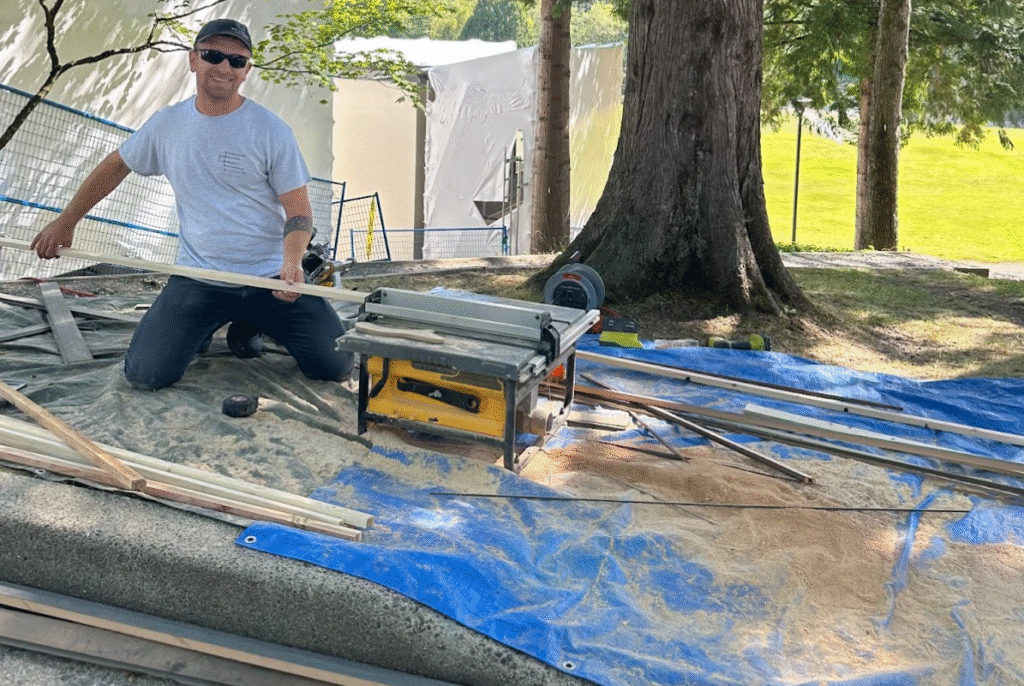 Man working on a roof renovation project, using a table saw on a blue tarp, surrounded by wood materials and tools, emphasizing safety and preparation for holiday decorations.