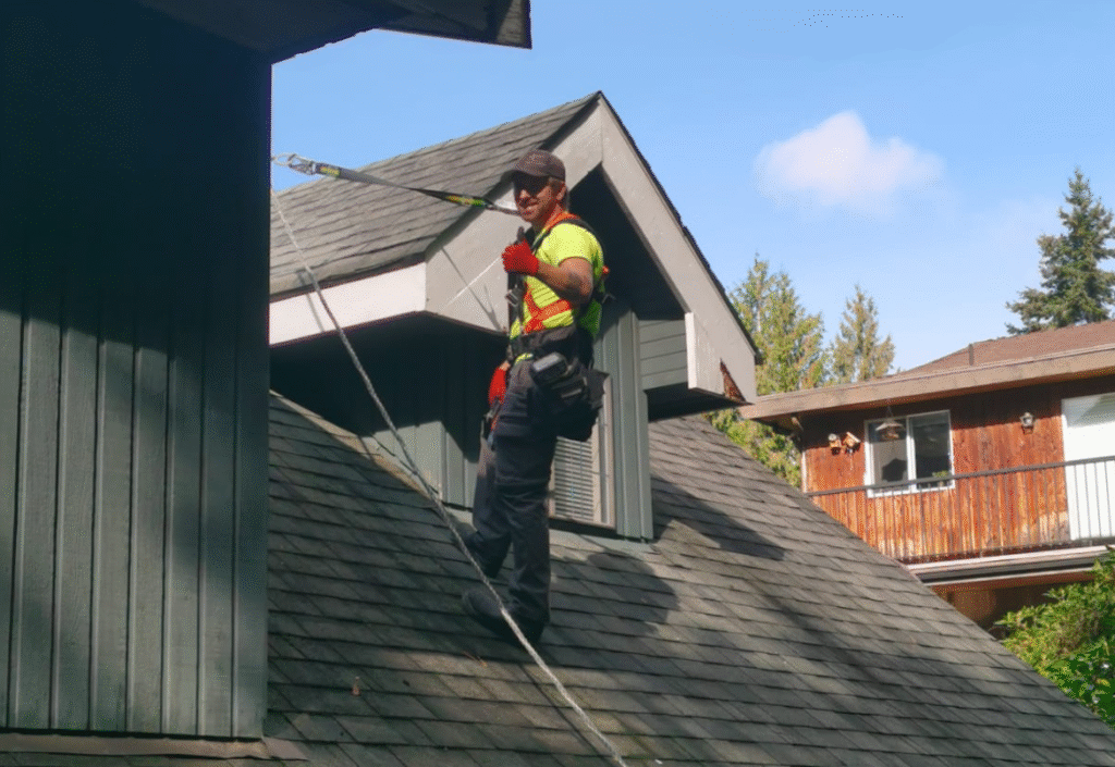Roofer in safety gear working on a sloped roof, emphasizing the importance of roof maintenance before hanging holiday lights.